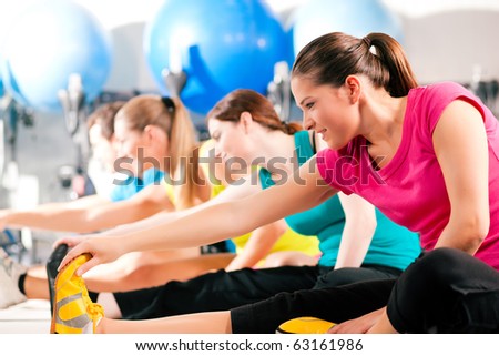 Group of four people in colorful cloths in a gym doing aerobics or warming up with gymnastics and stretching exercises