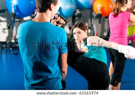 Woman Kick boxer kicking her trainer in a sparring session, in the background other boxers are hitting the sandbag