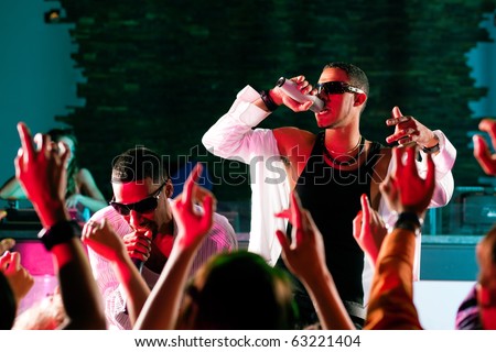 Rap or Hip-Hop Musicians performing on stage in a club in front of a cheering crowd