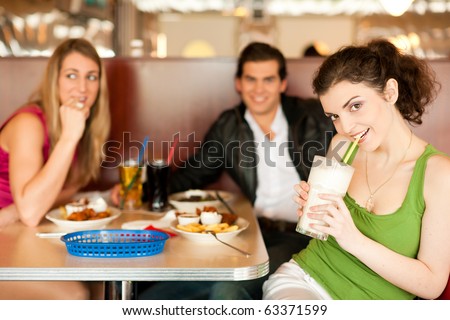 Three friends in a restaurant or diner eating fries and drinking milkshakes, shot with available light, very selective focus