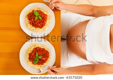 Eating for two - hungry pregnant woman with two servings of pasta Bolognese in front of her