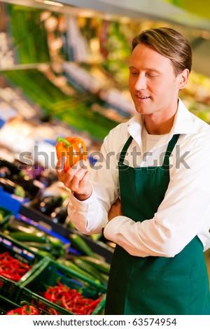 Shop assistant in a supermarket at the vegetable shelf checking the stuff for sale