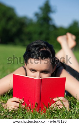 Woman reading book in the sunshine lying on a meadow in summer, FOCUS is on the book