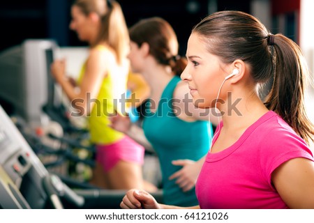 Running on treadmill in gym - group of women exercising to gain more fitness, the woman in front wears earplugs and enjoys music