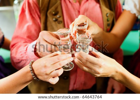 People in Bavarian Tracht clinking glasses with hard liquor in a pub