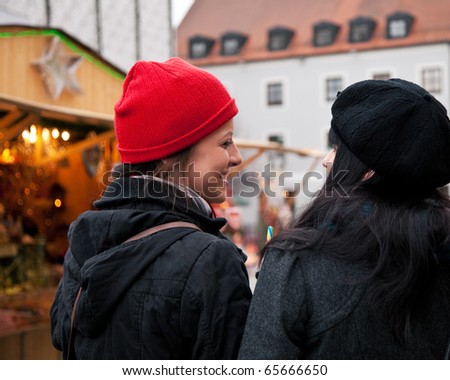 Two women strolling over Christmas market in front of a booth, it is cold