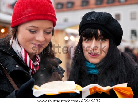 Two women on Christmas market eating crepes - a special kind of pancake - in front of a booth, it is cold