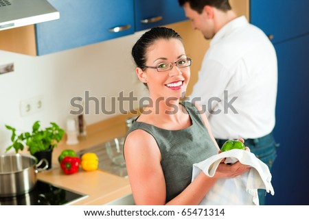 Young couple - man and woman - cooking in their kitchen at home cleaning vegetables