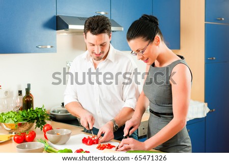 Young couple cooking - man and woman in their kitchen at home preparing vegetables for salad and pasta sauce