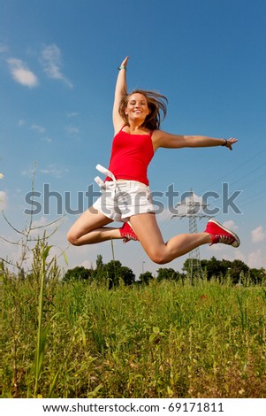 Woman in red t-shirt jumping high on a summer meadow under a blue sky, in the background a power pole is to be seen
