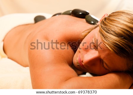 man in wellness and spa setting having a hot stone therapy session