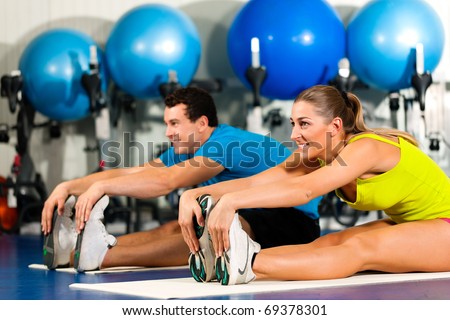 couple in colorful cloths in a gym doing aerobics or warming up with gymnastics and stretching exercises