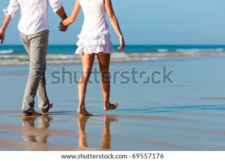 Couple in vacation having a walk on beach in summer, only torso to be seen, they are holding hands