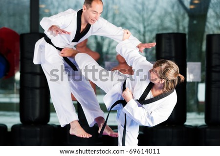 People in a gym in martial arts training exercising Taekwondo, both have a black belt