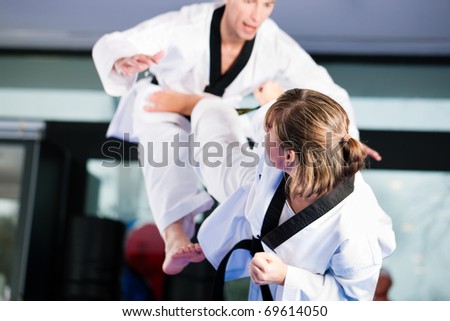 People in a gym in martial arts training exercising Taekwondo, both have a black belt