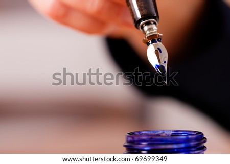 person (only hand to be seen) writing a letter on paper with a pen and ink, in the foreground there is an ink pot