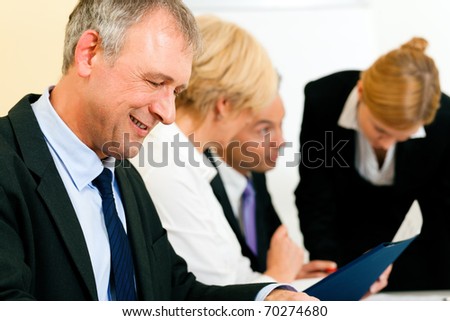 Small business team in the office in front of a whiteboard discussing a project and some documents
