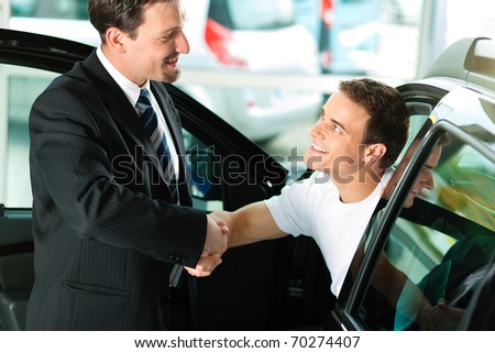 Man buying a car in dealership sitting in his new auto, the salesman talking to him and explaining details