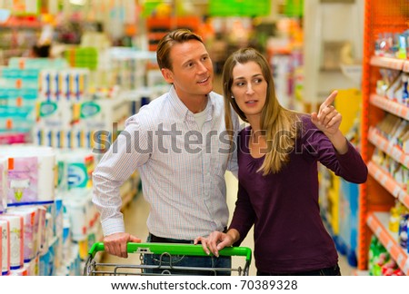 Couple in a supermarket shopping equipped with a shopping cart buying groceries and other stuff, they are looking for what they need
