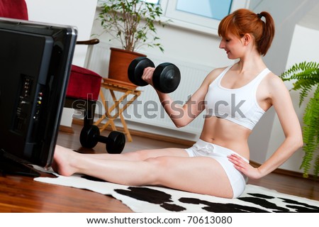 Woman is exercising with weights in her living room watching a fitness video
