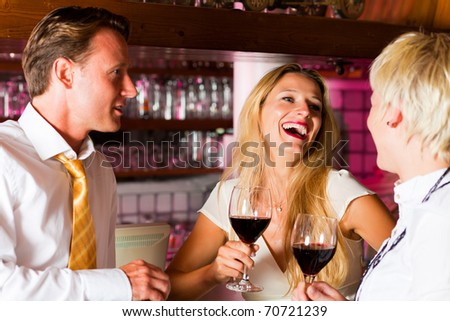 Man and two women in a hotel bar in the evening having glasses of red wine and probably a little flirt
