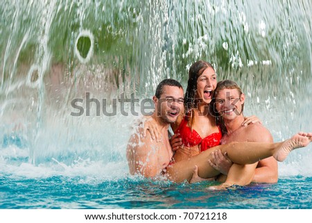 Three young people - woman and two men - at a public swimming pool standing under a water gadget