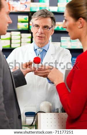 Pharmacist with customers in pharmacy, he is holding a bottle with pharmaceuticals in his hand