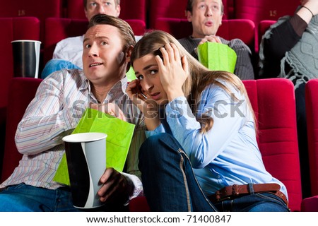 Couple in cinema watching a movie; it seems to be a horror movie