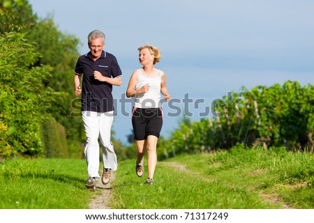 Mature or senior couple doing sport outdoors jogging down a path in summer Mature or senior couple doing sport outdoors jogging down a path in summer