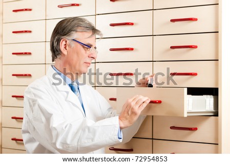 Pharmacist in front of medicine chest is looking for some medicine