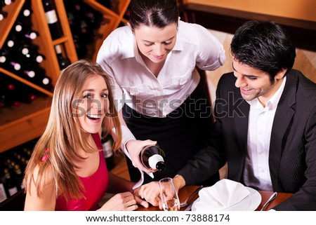 Waitress in a fancy restaurant filling glasses of couple with champagne
