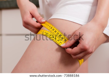 Thin woman measuring her thigh with a tape measure, only the thigh to be seen