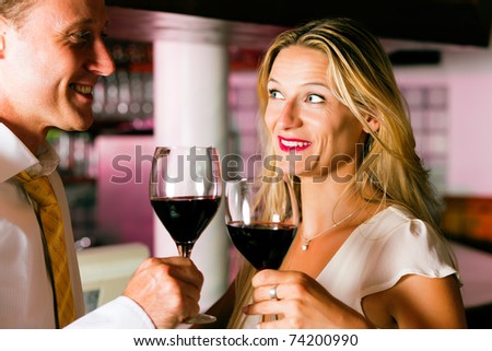 Man and woman in a hotel bar in the evening having glasses of red wine and a little flirt