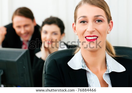 Small business team working in the office on their monitors or laptops in a shared project; one woman is looking in the camera