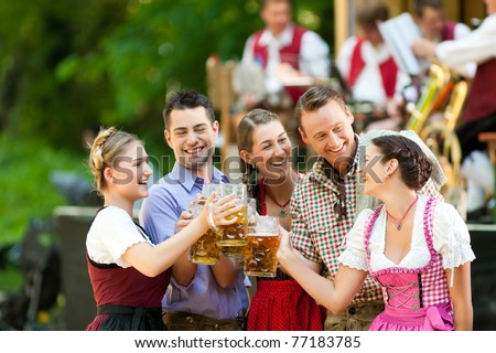 In Beer garden in Bavaria, Germany - friends in Tracht, Dindl and Lederhosen and Dirndl standing in front of band