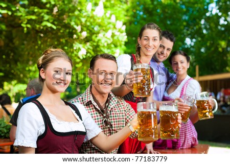 In Beer garden - friends in Tracht, Dindl and Lederhosen drinking a fresh beer in Bavaria, Germany