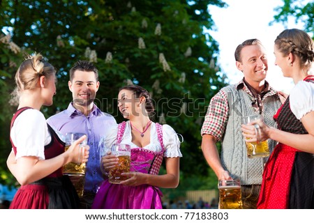 In Beer garden - friends in Tracht, Dindl and Lederhosen drinking a fresh beer in Bavaria, Germany