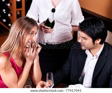 Waitress in a fancy restaurant filling glasses of couple with champagne