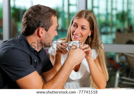 Young couple - man and woman - drinking coffee in a cafe in front of a glass facade