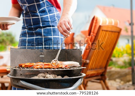 Happy family having a barbecue in summer; father stands next to the fire