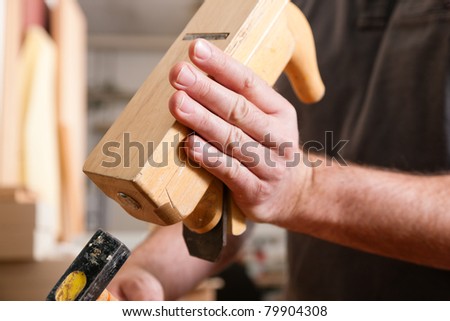 Carpenter working with a planer in his workshop, close up on the tool with hands