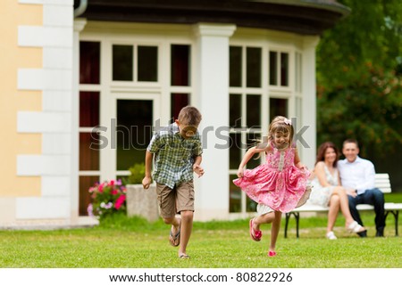Young happy family - the children are playing and the parents sitting in the sun on a bench in front of their villa
