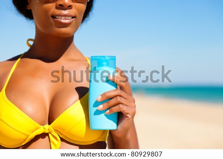 Woman in yellow bikini offering suncream on the beach in order to avoid sunburn, lots of copyspace