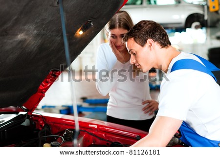 Woman talking to a car mechanic in his repair shop, both are standing next to the car