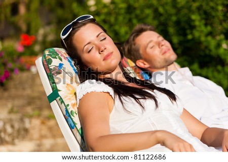Happy couple - a man and a woman - resting in a deck chair in summer
