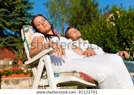 Happy couple - a man and a woman - resting in a deck chair in summer