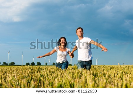 Happy couple running over grainfield in summer hand in hand