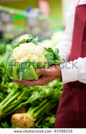 Man - only hands to be seen - in supermarket as shop assistant; he is carrying a cauliflower