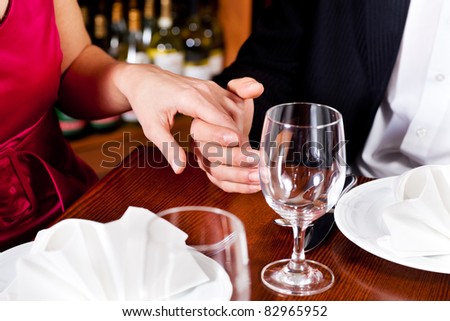 Couple, just hands to be seen, is holding hand while waiting for their food and drinks in a restaurant.
