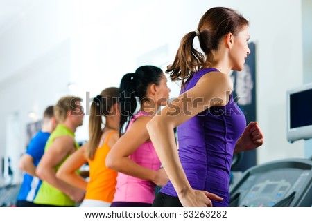 Running on treadmill in gym or fitness club - group of women and men exercising to gain more fitness